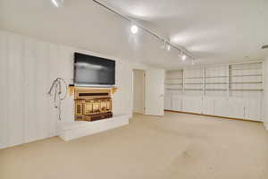 Unfurnished living room featuring light carpet, track lighting, a textured ceiling, and built in shelves