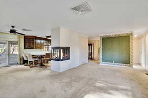 Interior space featuring ceiling fan, a multi sided fireplace, ornamental molding, and carpet floors