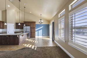 Kitchen with light tile patterned flooring, a breakfast bar area, an inviting chandelier, decorative light fixtures, and stainless steel refrigerator