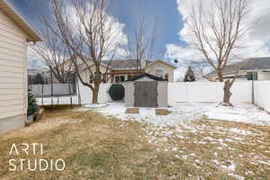 Yard covered in snow featuring a trampoline and a shed