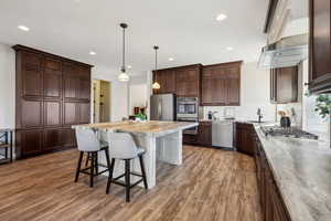 Kitchen with hardwood / wood-style flooring, appliances with stainless steel finishes, hanging light fixtures, backsplash, and a center island