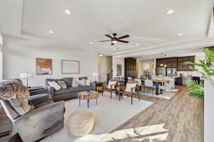 Living room with a raised ceiling, ceiling fan, and light wood-type flooring