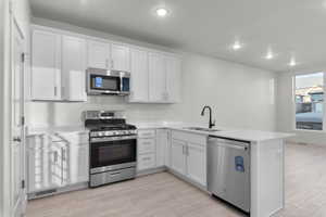 Kitchen featuring sink, light hardwood / wood-style flooring, appliances with stainless steel finishes, kitchen peninsula, and white cabinets