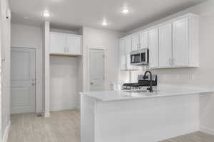 Kitchen featuring white cabinetry, light hardwood / wood-style flooring, kitchen peninsula, and appliances with stainless steel finishes