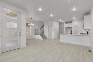 Interior space featuring sink, white cabinets, a chandelier, hanging light fixtures, and light wood-type flooring