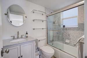 Full bathroom with vanity, bath / shower combo with glass door, and toilet