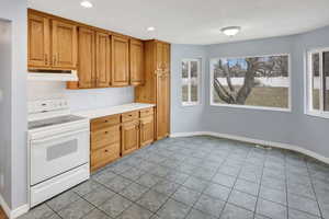 Kitchen featuring light tile patterned floors, white electric stove, and a healthy amount of sunlight