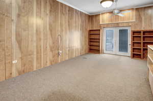 Unfurnished living room featuring french doors, ornamental molding, carpet floors, and wood walls