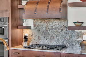 Kitchen with stainless steel appliances, exhaust hood, and decorative backsplash