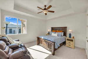 Bedroom featuring light colored carpet, a ceiling fan, visible vents, a raised ceiling, and baseboards
