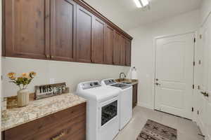 Washroom with light tile patterned floors, visible vents, cabinet space, washer and dryer, and a sink