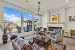 Tiled living room featuring an inviting chandelier, a glass covered fireplace, visible vents, and plenty of natural light