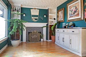 Interior space with a brick fireplace, a textured ceiling, and light hardwood / wood-style floors