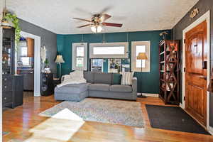 Living room with ceiling fan, a textured ceiling, and light hardwood / wood-style floors