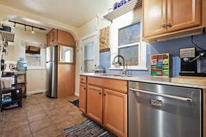 Kitchen with sink, backsplash, light tile patterned floors, and appliances with stainless steel finishes