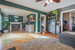 Living room with ceiling fan, wood-type flooring, a brick fireplace, and a textured ceiling