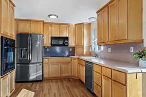 Kitchen with tasteful backsplash, sink, black appliances, light brown cabinets, and light hardwood / wood-style flooring