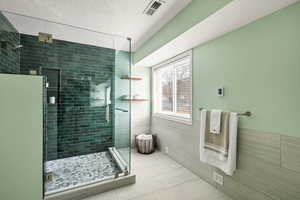 Bathroom with tile walls, an enclosed shower, and a textured ceiling