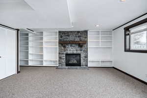 Unfurnished living room featuring a stone fireplace, carpet floors, built in features, and a textured ceiling