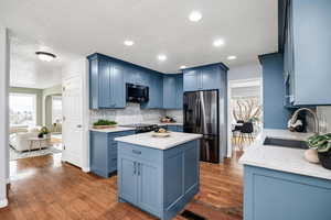 Kitchen featuring blue cabinets, tasteful backsplash, sink, stainless steel fridge, and a center island