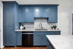 Kitchen featuring dishwashing machine, sink, dark hardwood / wood-style floors, blue cabinets, and decorative backsplash