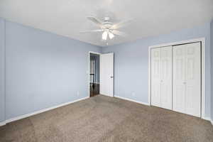 Unfurnished bedroom with carpet, a textured ceiling, ceiling fan, and a closet