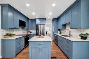 Kitchen with sink, dark wood-type flooring, appliances with stainless steel finishes, a center island, and blue cabinets