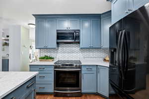 Kitchen with sink, appliances with stainless steel finishes, dark hardwood / wood-style flooring, light stone countertops, and backsplash