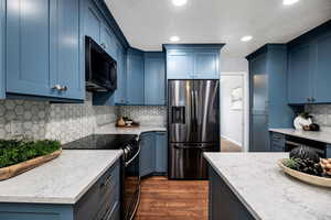 Kitchen featuring stainless steel refrigerator with ice dispenser, blue cabinets, and black electric range oven