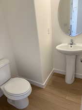 Half bathroom featuring a sink, toilet, baseboards, and wood finished floors