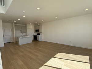 Unfurnished living room featuring recessed lighting, visible vents, light wood-style floors, a sink, and baseboards