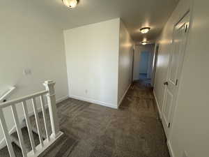 Hallway with baseboards, dark carpet, and an upstairs landing