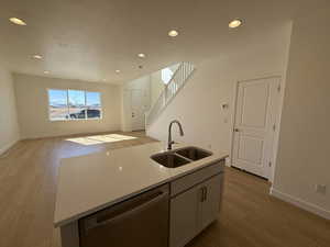 Kitchen featuring light stone counters, open floor plan, a kitchen island with sink, a sink, and dishwasher