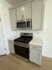 Kitchen with baseboards, appliances with stainless steel finishes, light wood-style flooring, and light stone countertops