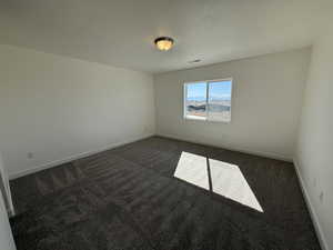 Spare room featuring dark colored carpet, visible vents, and baseboards