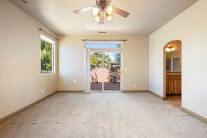 Empty room with arched walkways, light colored carpet, baseboards, and a ceiling fan