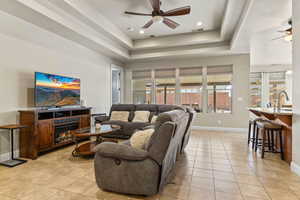 Living room featuring a raised ceiling, sink, light tile patterned floors, and ceiling fan