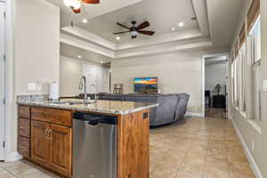 Kitchen with sink, a tray ceiling, kitchen peninsula, dishwasher, and light stone countertops