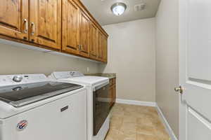 Washroom featuring cabinets, washing machine and dryer, and light tile patterned floors