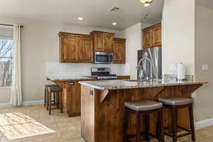 Kitchen with appliances with stainless steel finishes, a breakfast bar area, light stone counters, and kitchen peninsula