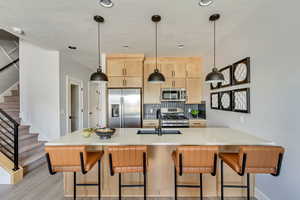 Kitchen featuring light brown cabinetry, a breakfast bar area, hanging light fixtures, kitchen peninsula, and stainless steel appliances