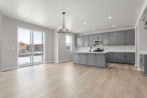 Kitchen featuring gray cabinetry, decorative light fixtures, an island with sink, and appliances with stainless steel finishes