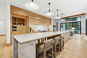 Kitchen featuring light brown cabinets, light stone counters, a large island with sink, and recessed lighting