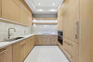 Kitchen featuring modern cabinets, light brown cabinetry, light stone countertops, stainless steel oven, and tasteful backsplash