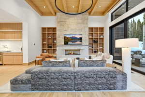 Living area featuring a wood ceiling with exposed beams, a towering ceiling, a fireplace, light wood finished floors, and built in shelves