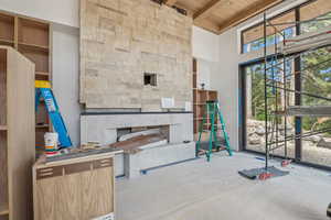 Unfurnished living room with a wood ceiling with exposed beams, a stone fireplace, and a towering ceiling