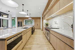 Kitchen featuring light stone counters, light brown cabinets, stainless steel appliances, modern cabinets, and recessed lighting