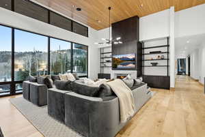 Living room with wooden ceiling, a warm lit fireplace, light wood-type flooring, a high ceiling, and recessed lighting