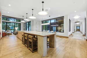 Kitchen featuring light wood-style flooring, light stone counters, pendant lighting, open floor plan, and a spacious island