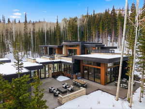 Snow covered back of property featuring a patio area, outdoor lounge area, and a forest view
